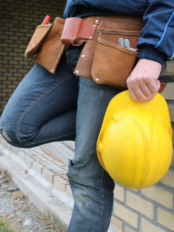 Handyman wearing a tool belt holding a yellow safety helmet